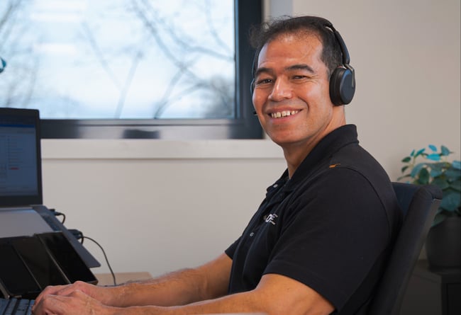 DHPS-medewerker met headset aan de telefoon achter zijn bureau DHPS-medewerker met headset aan de telefoon achter zijn bureau