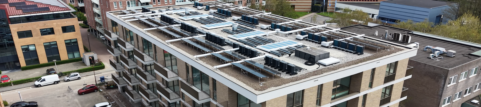 Luchtfoto van een appartementencomplex met tientallen warmtepomp-buitenunits en zonnecollectoren op het dak Luchtfoto van een appartementencomplex met tientallen warmtepomp-buitenunits en zonnecollectoren op het dak